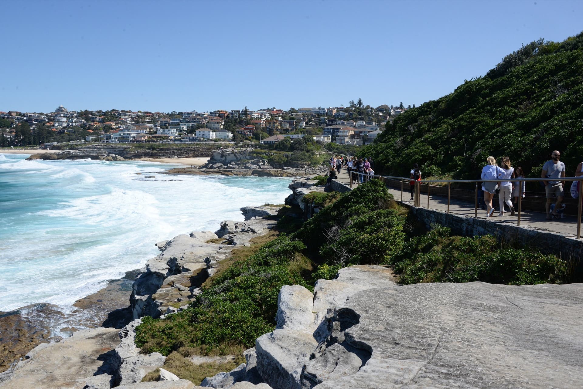 The Bondi to Tamarama coastal walk at Mackenzies Bay, walkers on the boardwalk above sandstone rocks and white surf