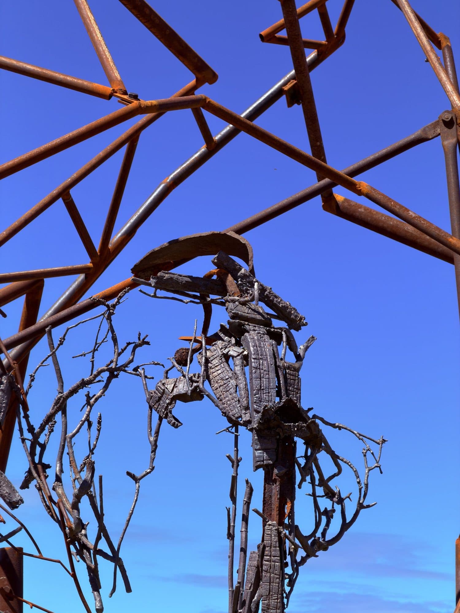 Looking up into Harrie Fasher's rust-coloured steel frame, with a figure of twisted bronze and branch-like forms suspended against the sky
